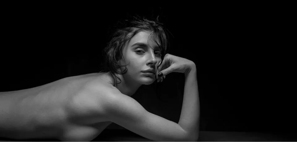 A side profile of a person lying on white sheets, demonstrating professional retouching of skin and fabric textures.