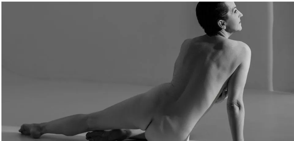 A seated woman viewed from behind in a soft grey studio setting, illustrating professional background management and tonal balance. nude professional photo retouching